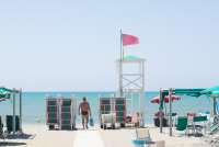 Bildet viser mann på veg til stranda i badebyen Tirrenia. Badevakten har heist det røde flagget. Solstoler står lagret klar for nye gjester.