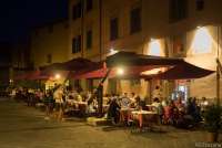Bildet viser folk som sitter ute og spiser på en av restaurantene på Piazza Dante Alighieri i Pisa. Bildet er tatt en varm sommerkveld og det er mørkt.