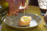 Bildet viser olivenolje som tømmes over en brødbit. Det er årets første olje som skal smakes. På en olivengård i Toscana.