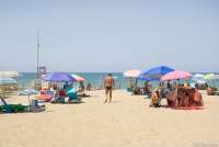 Bildet viser en mann som går ned mot stranda på Spiaggia Verruca i Tirrenia. På begge sider ligger folk under parasoller. Det er sol.