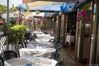 Bildet viser ledige bor på en av restaurantene i hovedgata i Tirrenia. I enden ser du et par som sitter og venter på servering.