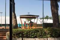 Bildet viser en mann og ei jente som sitter ved et bord under en pergola og prater. Ved tennisbanene i La Gabella ved Calci, Pisa.