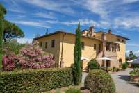 La Bella Lavanderina og Cavallino bak blomsterbusken. Rett frem er Cecco Bilenco og Staccia Buratta. Bilde av det ene feriehuset med ferieleiligheter. Sypress og blomstrende trær.