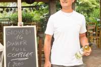 Verten Lamberto reklamerer for flere retters middag til 20 euro, inkludert vin! Foto av vertskapet ved vinbonden foran en plakat der restauranten på vingården inviteter til et italiensk middagsmåltid for 20 euro.