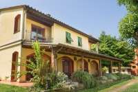 Bildet viser et av husene med terrasser, balkong, blomsterbed og plen. På feriebostedet La Pergola i Toscana. 