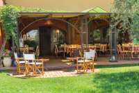 Bildet viser bord og stoler i solskinn, på uteserveringen foran restauranten på feriebostedet La Pergola, nært Pisa i Toscana.