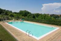 Bildet viser bassenget med hagen og en skyggefull pergola i bakgrunnen. På feriebostedet La Pergola med restaurant i Toscana. 