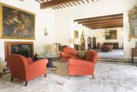 Bildet viser stue med sitteplasser foran peisen. Langbord i spisestua i bakgrunnen. Feriehus for grupper ved Pisa i Italia.