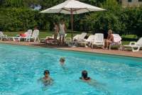 Bildet viser barnefamilie på ferie i Toscana som koser seg rundt bassenget ved feriehuset. 