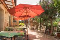 Bildet viser terrasse med uteplasser med bord, stoler og parasoller foran ferieleilighetene i hovedhuset på vingården Borgo Etruschi.