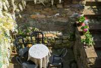 Uteplass ved inngangsparti. Hagen er ovenfor. Liten terrasse like ved inngangsdøra. Blomsterflor rammer inn uteplassen. Bilde.