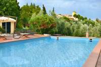 Bildet viser bassenget i Villa Alba og utsikt mot nærmeste landsby som ligger i gangavstand fra villaen. Ved bassengkanten står det en parasoll og stoler.