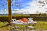 Bildet viser en av terrassene i Villa Alba. Et bord er dekket for kaffe og kaker. Utsikt mot åsene rundt. Det er sol og grønt.