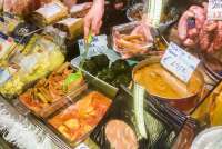 Bildet viser hånda til en ekspeditør som tar opp delikatesser med en øse i en disk i en matbutikk i landsbyen Calci.