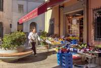 Bildet viser en kvinne utenfor en av nærbutikkene i Calci. Frukt og grønnsaker ligger utstilt  på bord.